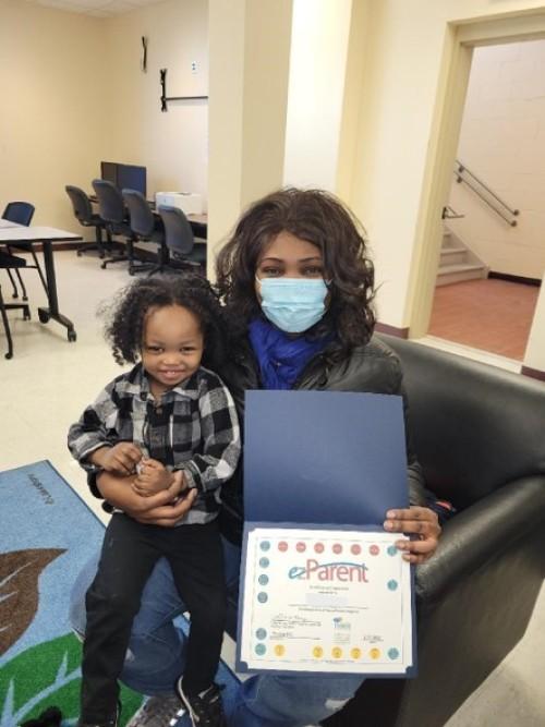 A mother holding up her completion certificate and her son.