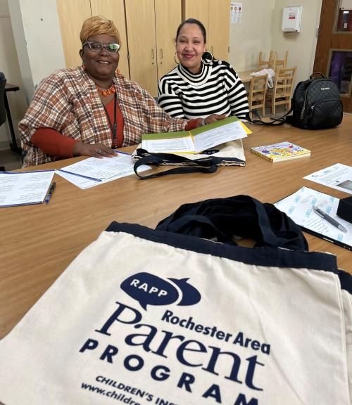 A facilitator and parent smile as they pick up their supplies. 