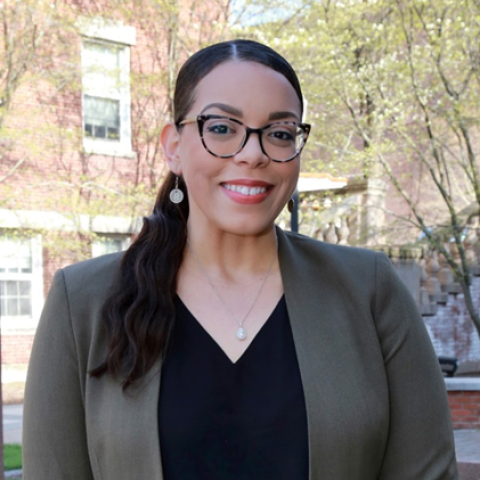 Woman of color with glasses and a low ponytail, dressed in a blazer.