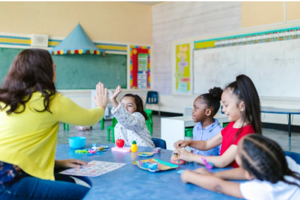 A classroom of kids listens to a teacher.